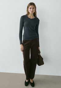 Haut à manches longues gris foncé avec un col en V, associé à un pantalon large marron. Texture douce, complété par des chaussures plates noires et un sac à main marron.