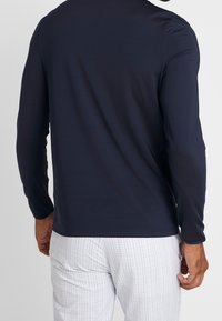 Marinblå långärmad skjorta med en slät textur. Har en enkel design och en kroppsnära passform. Matchas med rutiga vita byxor.