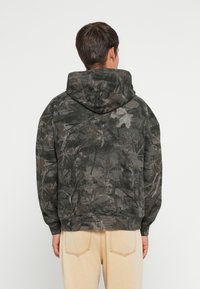 Mikina s kapucňou tmavosivej farby s camouflage vzorom listov. Vyrobená z mäkkej tkaniny, má voľný strih a rebrované manžety.