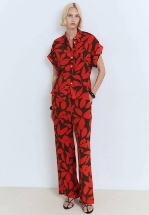 Set di camicia e pantaloni a maniche corte con un motivo rosso e marrone, caratterizzato da grandi disegni di foglie, texture liscia e bottoni sulla camicia.