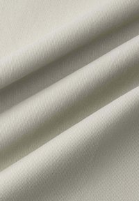 Gestructureerde stof in een lichtcrème kleur, met een fijn ribbelpatroon. Het materiaal vertoont zachte vouwen en een lichte glans, wat diepte en dimensie uitstraalt.