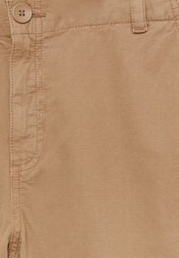 Pantalon en coton couleur sable avec fermeture à bouton, passants de ceinture et détail de couture apparente près de la taille et des poches.