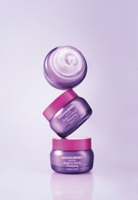 Trzy ułożone jeden na drugim słoiki kremu EquaBerry Bakuchiol Plumping Capsule. Słoiki są fioletowe z różowymi wieczkami, w górnym słoiku znajduje się widoczny krem.