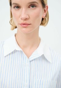 Camicia a righe blu e bianche con colletto classico e piccola tasca sul petto, caratterizzata da un tessuto leggero e morbido.