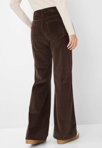Bruine flared corduroy broeken met een hoge taille, voorzien van achterzakken en een gladde textuur. Gecombineerd met beige platform schoenen.