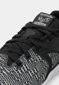 Čierne a šedé tenisky Reebok s textúrovaným sieťovinovým zvrškom, ktoré majú čierne šnúrky, logo na patke a mriežkový vzor po stranách.