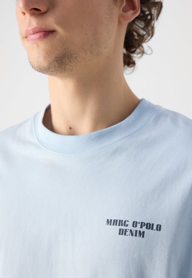 Himmelblaues Baumwoll-T-Shirt mit Rundhalsausschnitt und dem aufgedruckten Text "MARC O'POLO DENIM" in Dunkelblau nahe der linken Schulter.