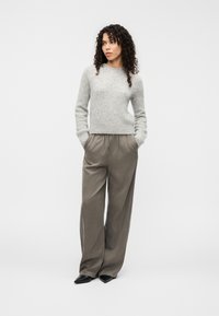 Gray knit sweater with a round neckline, paired with loose beige trousers and black pointed shoes, standing on a white background.