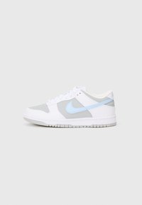 Bílé a šedé nízké tenisky se světle modrým Nike swoosh, bílými tkaničkami a perforovanou špičkou na jednobarevném pozadí.