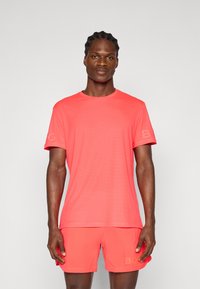 Men's athletic outfit featuring a short-sleeve, bright coral t-shirt and matching shorts, both made from lightweight, textured fabric.