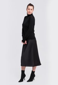 Un pull à col roulé noir associé à une jupe midi en satin noire. La tenue présente des manches ajustées et des talons hauts élégants et pointus.