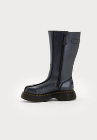 Bota alta de cuero negro con cremallera lateral, suela gruesa y detalle de costura naranja sobre fondo blanco.