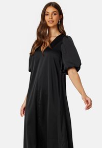Czarna satynowa sukienka z dekoltem w kształcie litery V, bufiastymi rękawami i zwiewną sylwetką, o gładkiej fakturze i minimalistycznym designie bez wzorów.