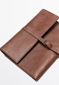 Braunes Leder-Notizbuchcover mit glatter Textur, ausgestattet mit einer Schnallenverschluss und genähten Akzenten. Gefaltetes Design, kompakte Form.