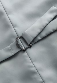 Un tissu gris avec une texture lisse comporte une boucle en métal et une sangle. Les coutures sont visibles le long des bords, mettant en valeur le détail du design.
