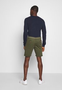Chemise à manches longues marine et short vert olive, avec des poignets roulés, deux poches arrière avec des coutures visibles et une ceinture tressée.