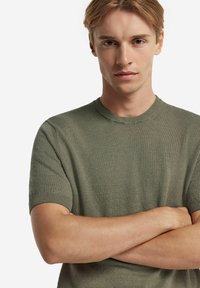 Olivgrön, stickad kortärmad tröja med rund halsringning och ribbade ärmslut, som har en lätt textur och en figurnära passform.