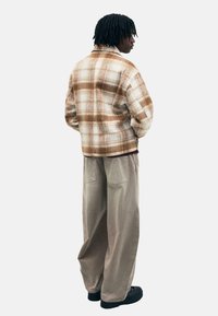 Hnedý a béžový károvaný kabát s mäkkou textúrou, spárovaný so voľnými béžovými kordovými nohavicami, zachytený zo zadného pohľadu.
