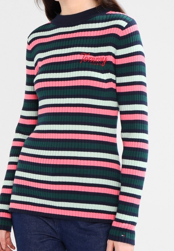 Femme portant un pull à manches longues côtelé avec des rayures horizontales en bleu marine, rose, vert clair et rouge, avec le logo "Tommy Jeans" sur la poitrine.