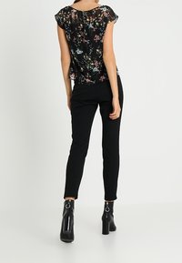 Czarna kwiecista bluzka z krótkimi falbaniastymi rękawami, zestawiona z dopasowanymi czarnymi spodniami i błyszczącymi czarnymi botkami na obcasie. Tkanina o fakturze i żywych kolorach.