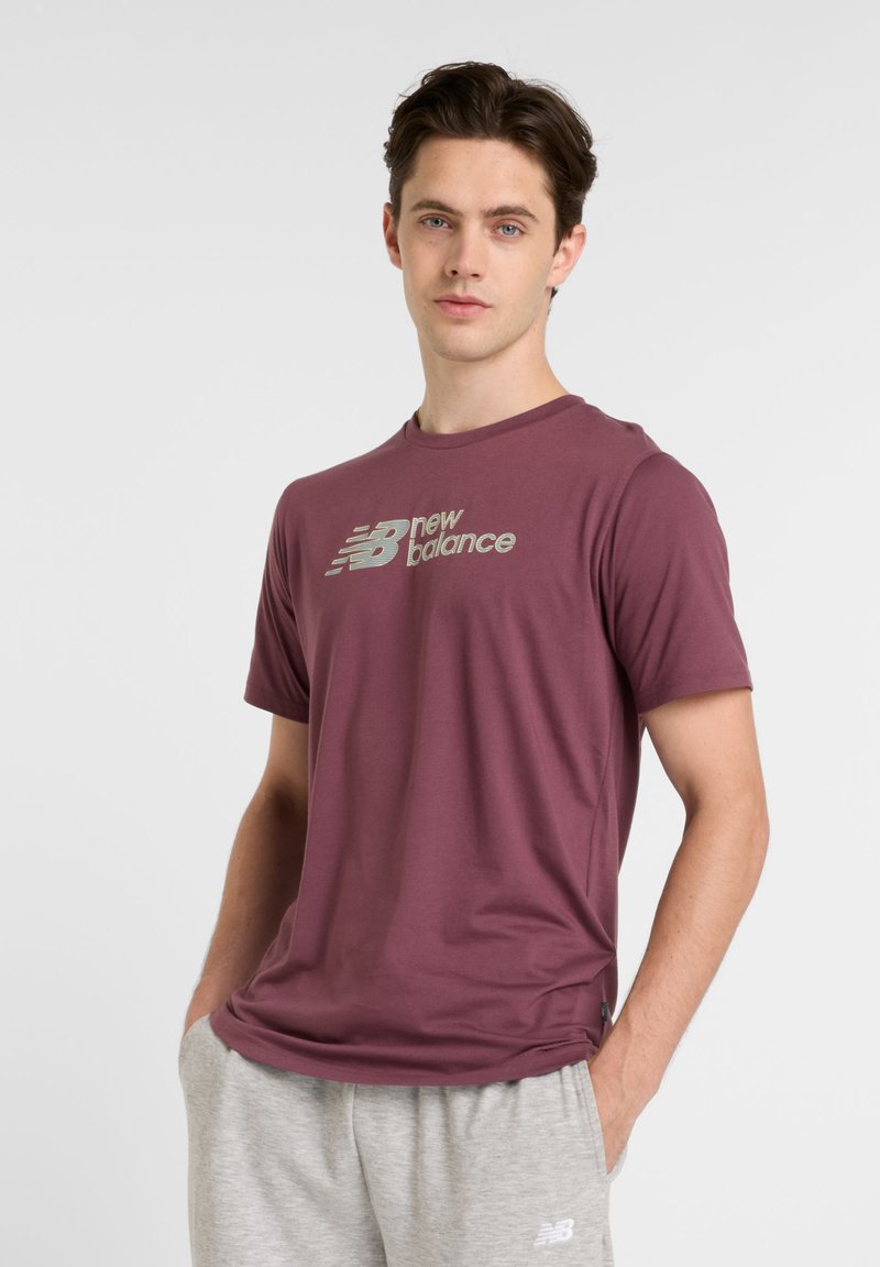 Bordo trumpas rankovės marškinėliai, pagaminti iš lygaus audinio, su atspindinčiu New Balance logotipu krūtinės srityje. Derinami su pilkais sportiniais kelnais.