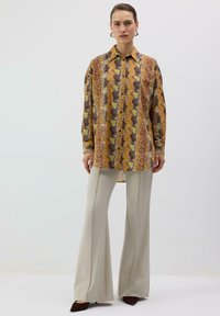 Chemise à manches longues avec col et motif serpent multicolore en or, marron et vert ; associée à un pantalon évasé beige clair.