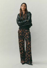 Fekete bőr bombázódzseki cipzárral, barna leopárdmintás, bő szárú nadrággal párosítva. Bevon fényes textúrával és derékrészen húzózsinórral.