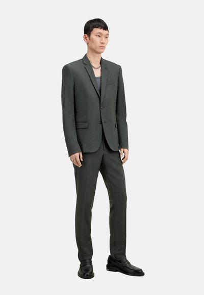 Completo grigio carbone con giacca aderente dotata di chiusura a un bottone, tasche piatte e pantaloni affusolati abbinati con una texture liscia.
