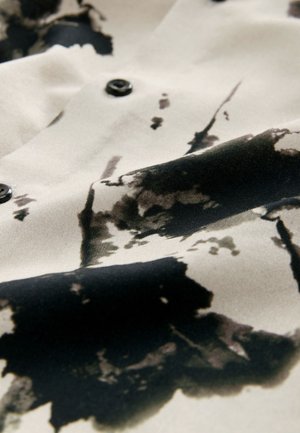 Satiinriie, millel on beež taust mustade ja tumehallide abstraktsete mustritega. Disaini täiustavad märkimisväärsed mustad nööbid.