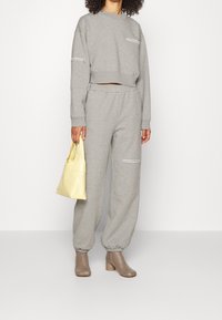 Grå kortärmad sweatshirt med kontrasterande sömmar, parat med grå joggers med elastiska muddar, och accessoriserat med en gul handväska och beige stövlar.