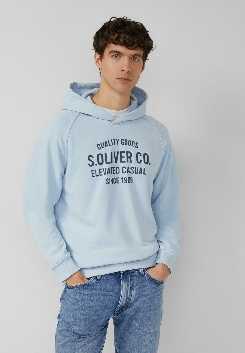 Hellblaues Sweatshirt mit Kapuze, vorne mit einem dunkelblauen, aufgedruckten Logo. Weicher Stoff mit gerippten Bündchen und Saum, kombiniert mit blauen Jeans.