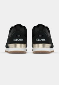 Czarne buty sportowe z teksturowaną cholewką, złotymi akcentami na pięcie i białą środkową podeszwą. Logo Skechers widoczne na zapiętce.