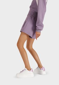 Pantaloni corti viola con vita alta e tasche. Sneakers bianche con dettagli viola e suola spessa. Tessuto morbido, design casual.