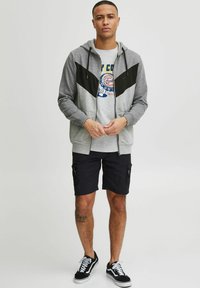 Grey zip-up hoodie with black accents, paired with a graphic gray t-shirt and black cargo shorts. Black sneakers complete the look.