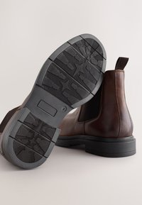 Hnedé kožené chelsea členkové topánky s elastickými bočnými panelmi, čierne gumové podrážky s textúrovaným vzorom pre lepšiu priľnavosť a pevná záložka na zadnej strane.