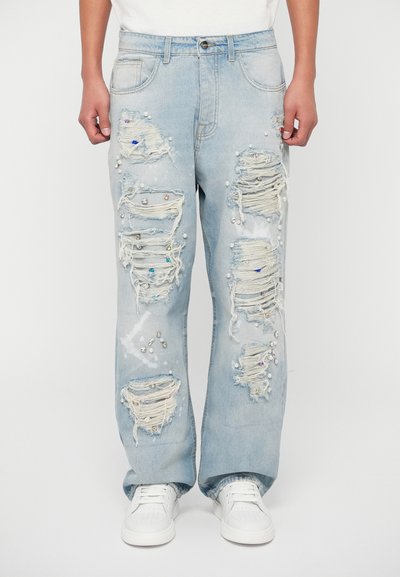 Svijetloplave traperice s izrezanim dijelovima, isfriganim rubovima i raspršenim kamenčićima. Dizajn ravnih nogavica s džepovima.