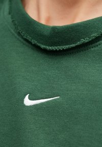 Πράσινο βαμβακερό μπλουζάκι με στρογγυλή λαιμόκοψη, με φθαρμένο γιακά και λευκό λογότυπο Nike Swoosh στο κάτω αριστερό μέρος.