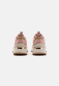 Tennarit, joissa on vaaleanpunaisen ja beigen sävyinen muotoilu, mokkanahkaa ja verkkomateriaaleja, kultaisia yksityiskohtia ja kiillotettu pohja. Brändäys näkyy kantapäässä.