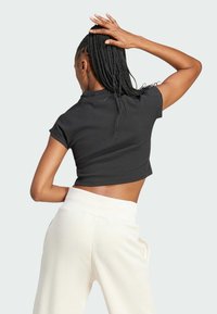 Black fitted crop top with short sleeves and ribbed texture, paired with cream wide-leg pants, showing the back view.
