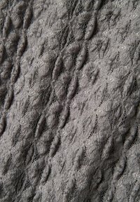 Tissu gris texturé avec des motifs ovales en relief et répétitifs. Matériau doux et tricoté avec une finition légèrement floue.