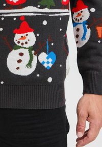 Suéter negro de punto con diseños coloridos de muñecos de nieve, gorros rojos, bufandas verdes, copos de nieve y un adorno en forma de corazón azul. Textura suave, puños acanalados.