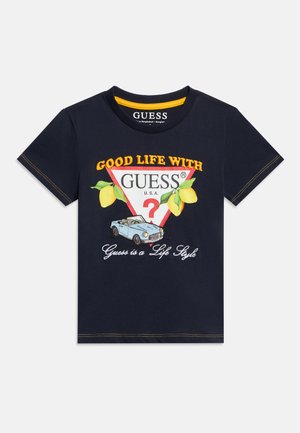 Marineblå t-shirt med teksten "Good Life with GUESS", gule citroner, en rød trekantslogo, en blå vintage kabrioletbil og teksten "Guess is a Life Style".