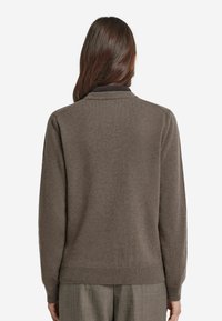 Brun stickad tröja med ribbad nederkant och ärmslut, med en klassisk kragdesign. Mjuk textur, lätt material.