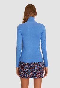 Lichtblauwe turtleneck trui met lange mouwen, ribgebreide hals, gladde textuur, gecombineerd met een mini-jurk met een multikleurige bloemenprint.