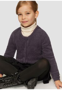 Lila, flauschige verkürzte Strickjacke mit V-Ausschnitt und fünf Knöpfen, getragen über einem cremefarbenen Rollkragenpullover. Kombiniert mit schwarzen Leggings und glänzenden Stiefeln.