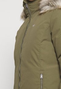 Giacca parka verde oliva con chiusura a zip e dettagli in finta pelliccia sul cappuccio. Materiale in poliestere con una texture liscia.