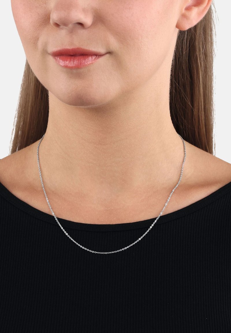 Donna che indossa una sottile collana d'argento sopra un top nero a coste, mostrando il collo, le clavicole e parte del viso inferiore.