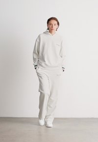 White hooded sweatshirt and matching sweats, with ribbed cuffs and waistbands. Simple design with subtle branding, worn with white sneakers.