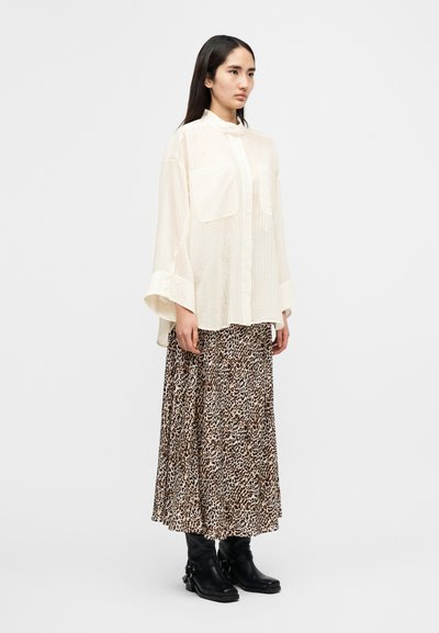 Ελαφρύ, εκρού μπλουζάκι με γιακά και δύο μπροστινές τσέπες, συνδυασμένο με μια ρέουσα φούστα με λεοπάρ σχέδιο και μαύρα μποτάκια αστραγάλου.