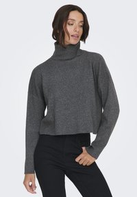 Maglione a collo alto tagliato, in tessuto a maglia grigio scuro; presenta maniche lunghe, leggermente oversized e una vestibilità rilassata. Abbinato a pantaloni neri.